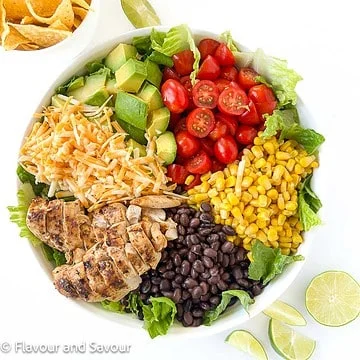 Overhead view of ingredients for chopped chicken taco salad in sections in a shallow white serving bowl.