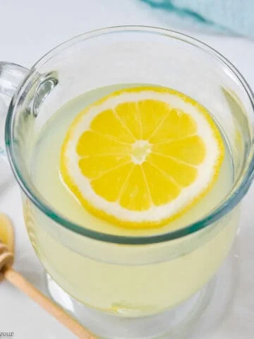 A glass mug of lemon ginger tea with a lemon slice.