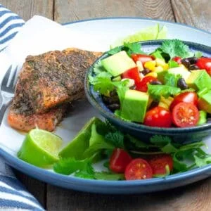 Jerk salmon and black bean salad on a plate with lime wedges.