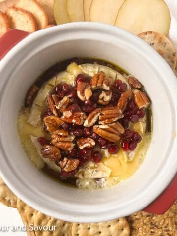 Square image of baked Brie cheese in a baking dish surrounded by crackers and sliced pears.