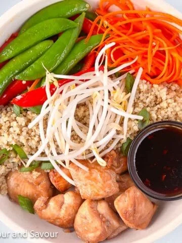 Teriyaki chicken cubes with quinoa, sugar snap peas, red pepper strips, julienned carrots, bean sprouts and a small bowl of teriyaki sauce.