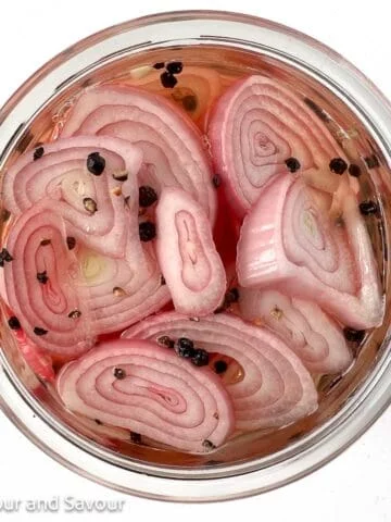 Pickled shallots in a jar with peppercorns.