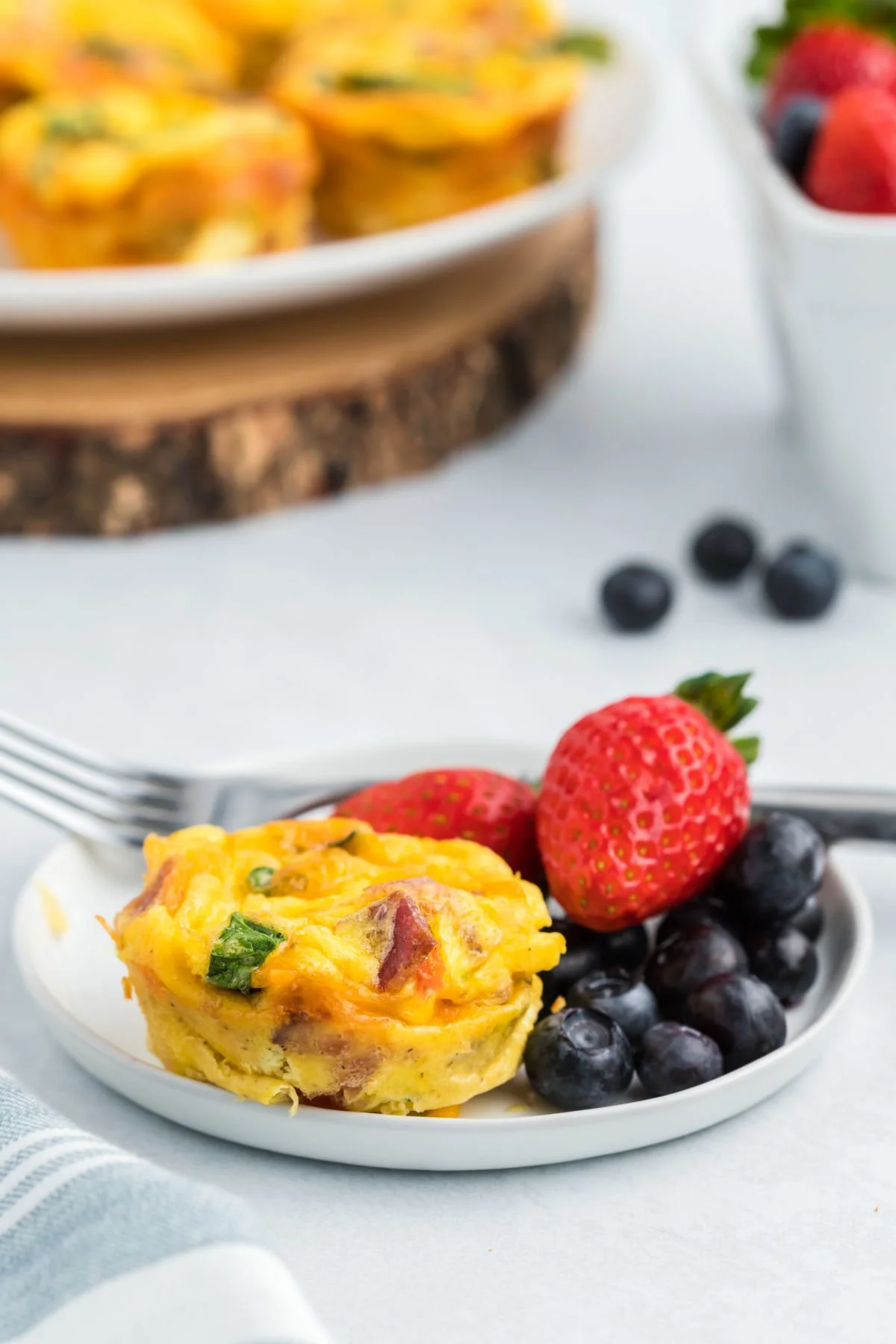 Egg bite with spinach and bacon on a plate with fresh berries.